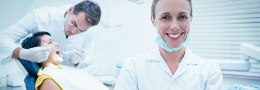 Dentist attends patient while dental assistant smiles at viewer